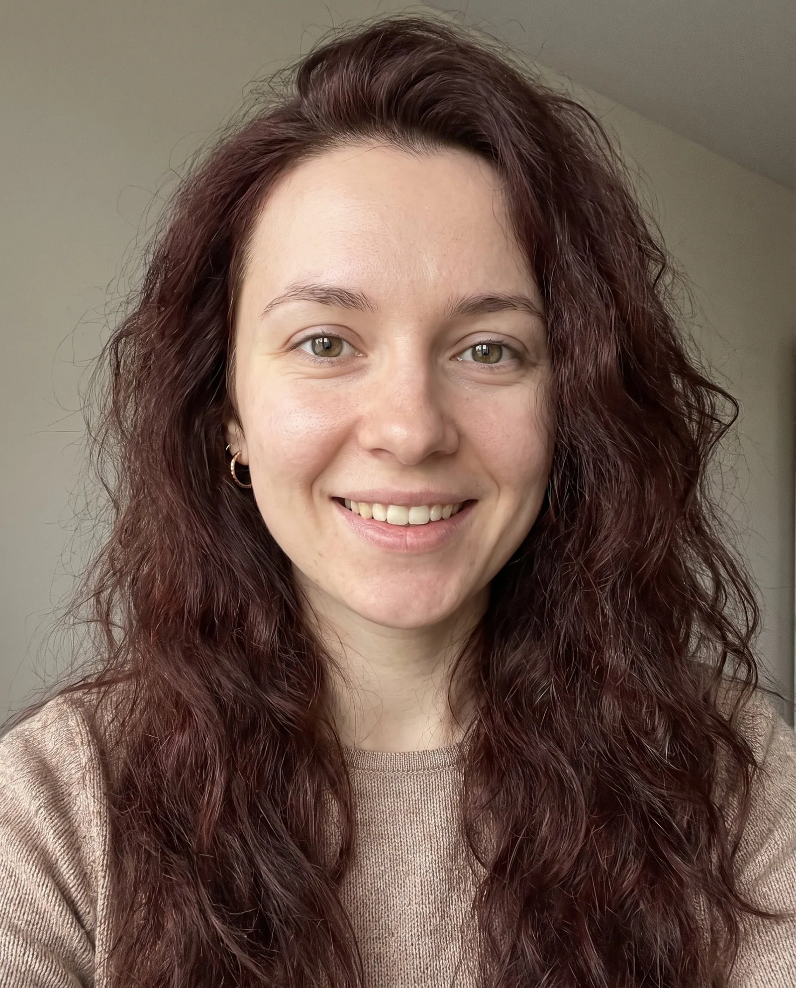 Solomiya, an adult AI character, smiling in a close selfie with long wavy auburn hair and a beige sweater